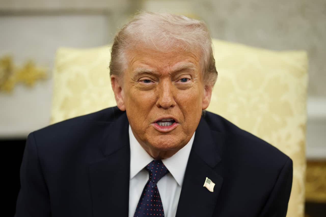 Donald Trump, wearing a dark blazer with an American flag pin on it, sitting in a yellow chair.