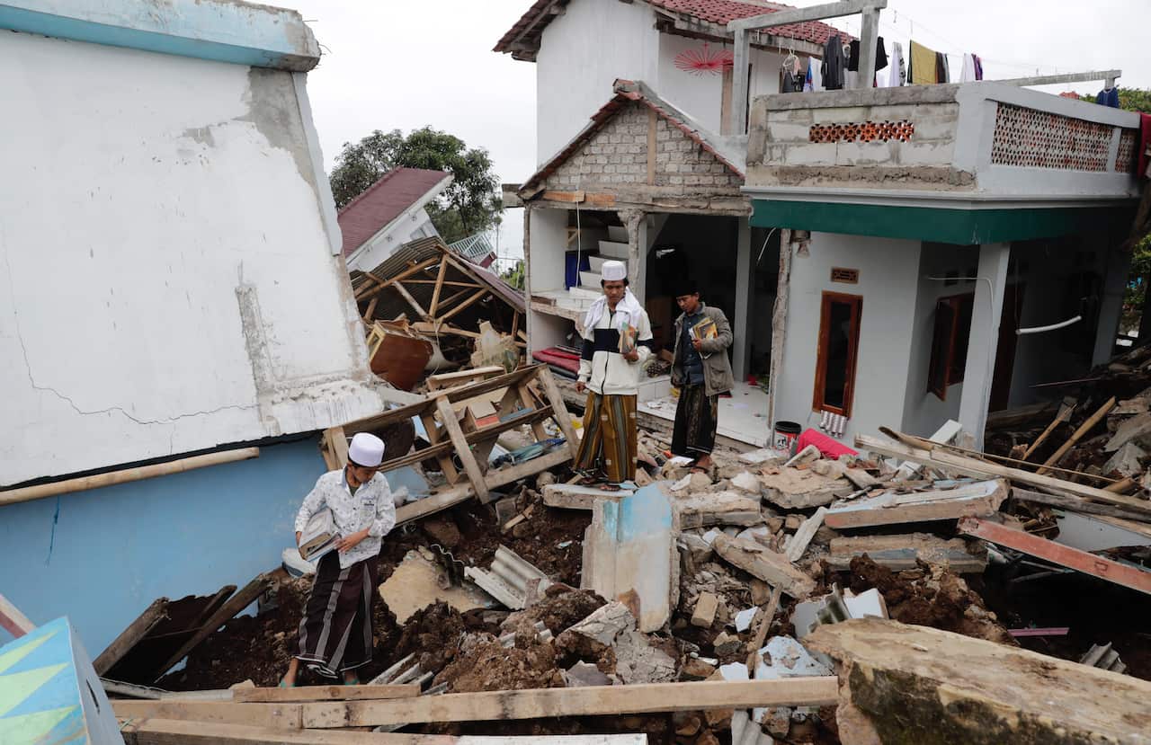 Collapsed building and debris lined the streets in Cianjur with three people standing amid ruins.