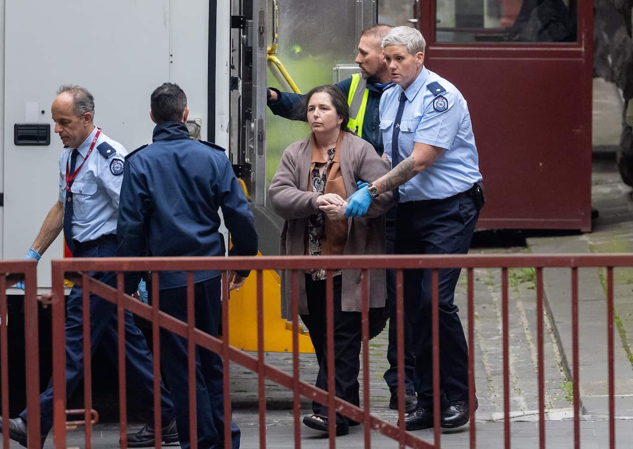 A woman being escorted by police officers out of a van