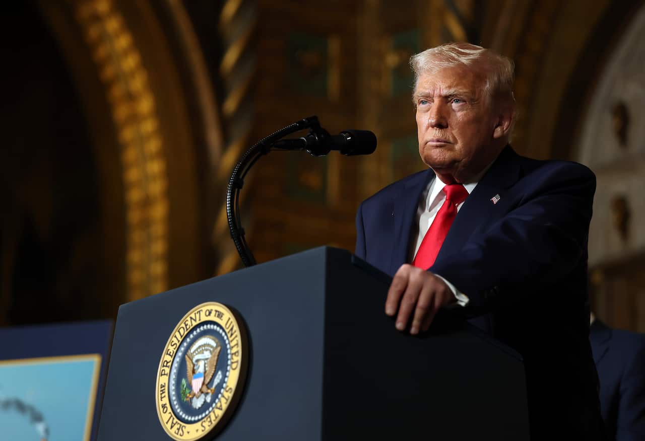 Trump with a serious expression speaking from a podium with the presidential seal