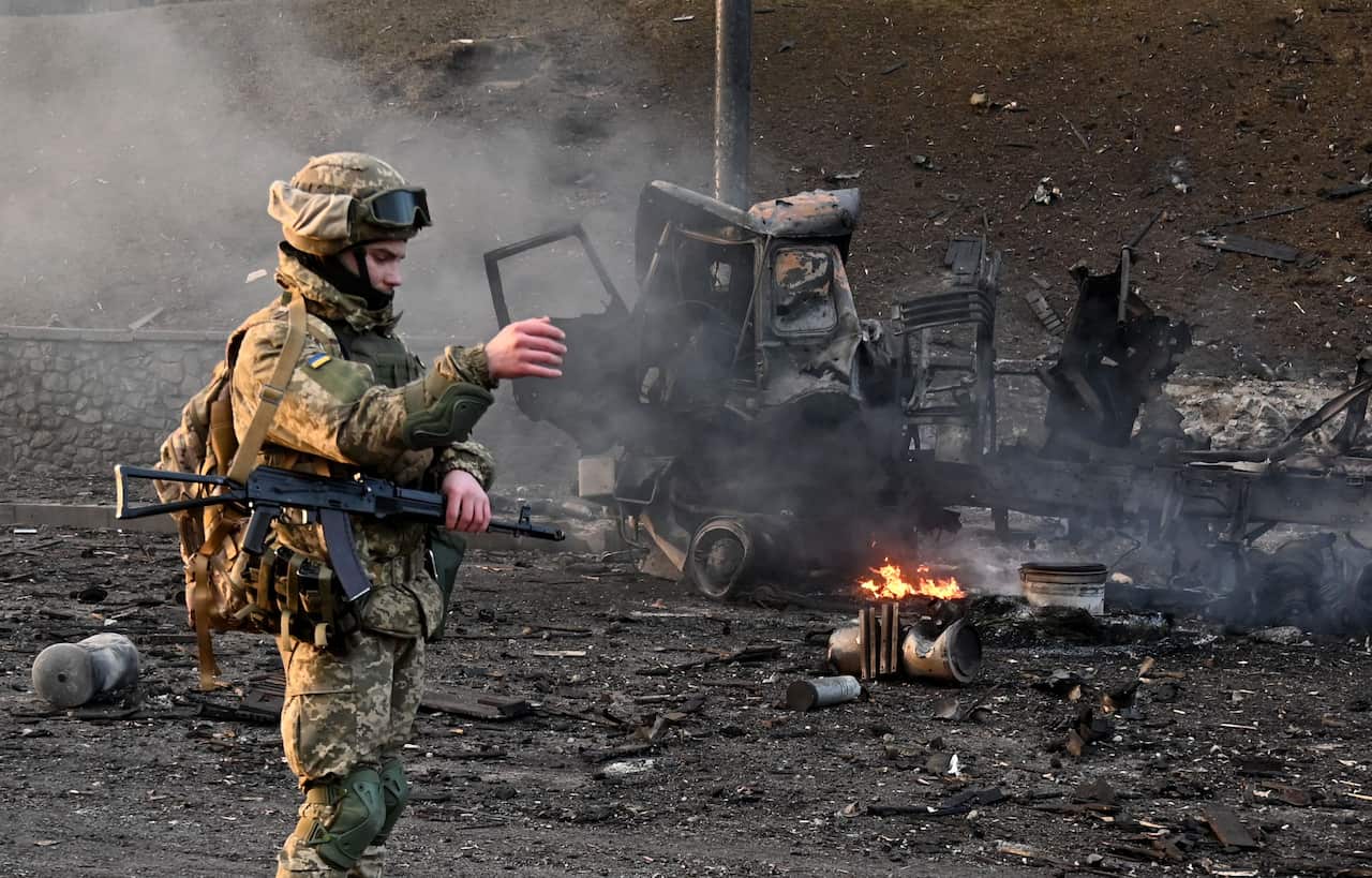 A soldier stands in front of a wrecked car