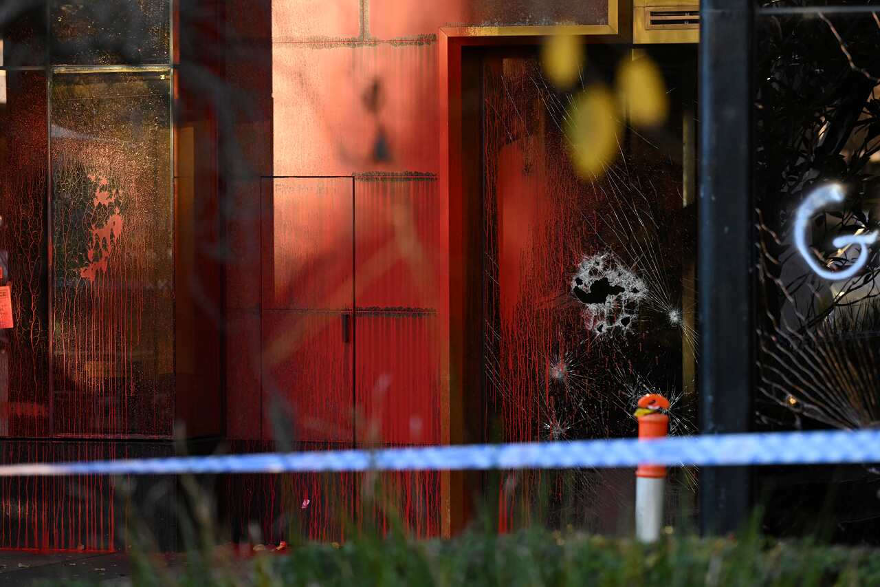 A building with smashed glass windows and red paint on it. Police tape is in front of it.