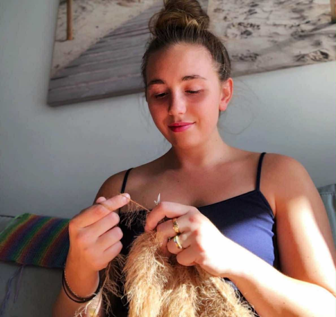 A young woman wearing a navy camisole is knitting.