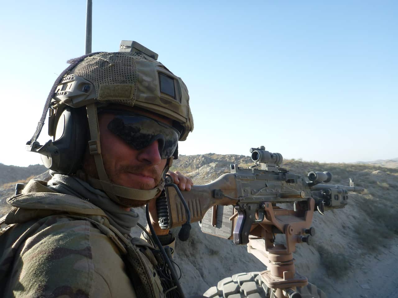 A man wearing sunglasses and an Australian military uniform with a gun 
