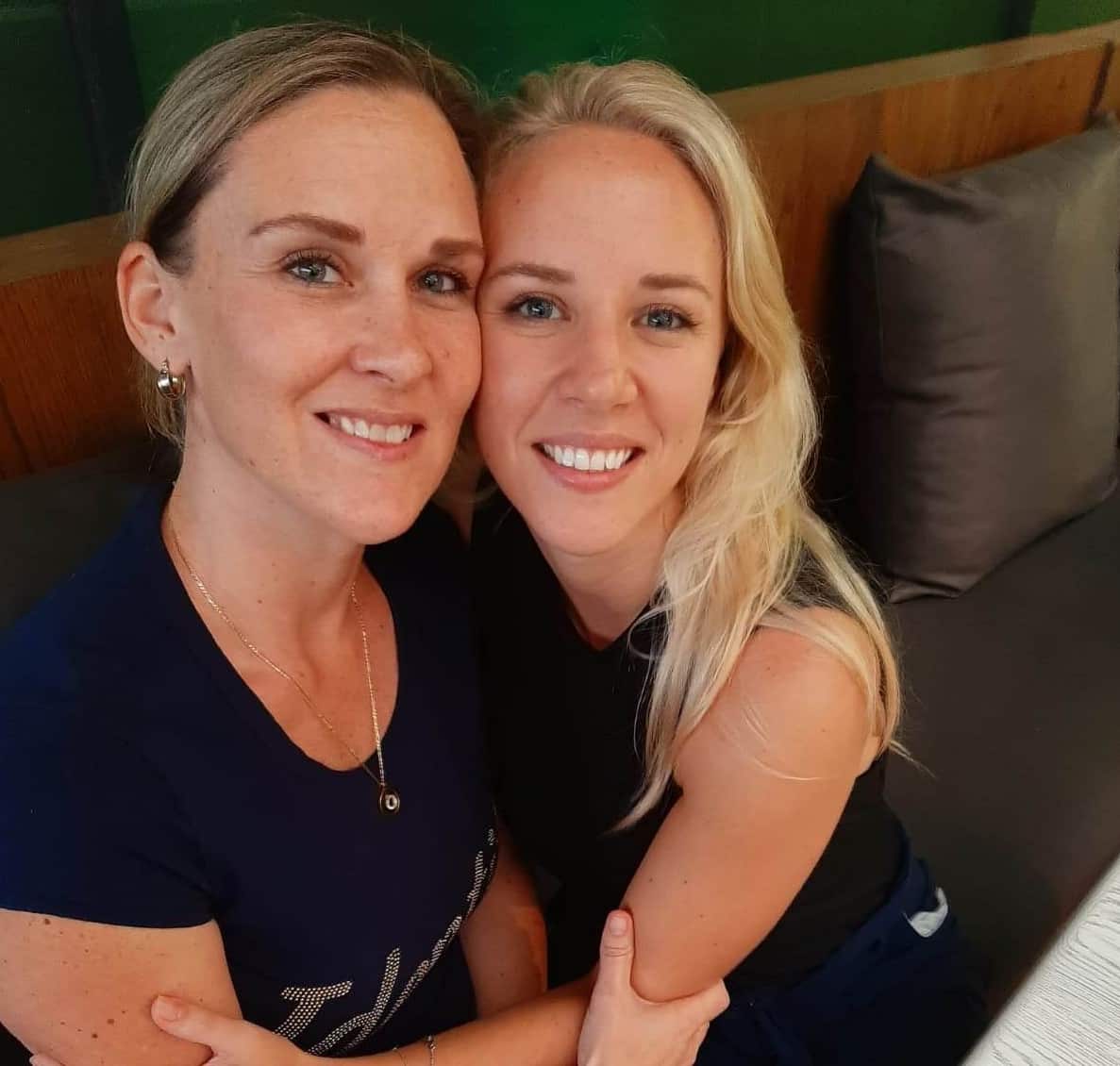 Two women wearing black tops sitting close together on a couch 