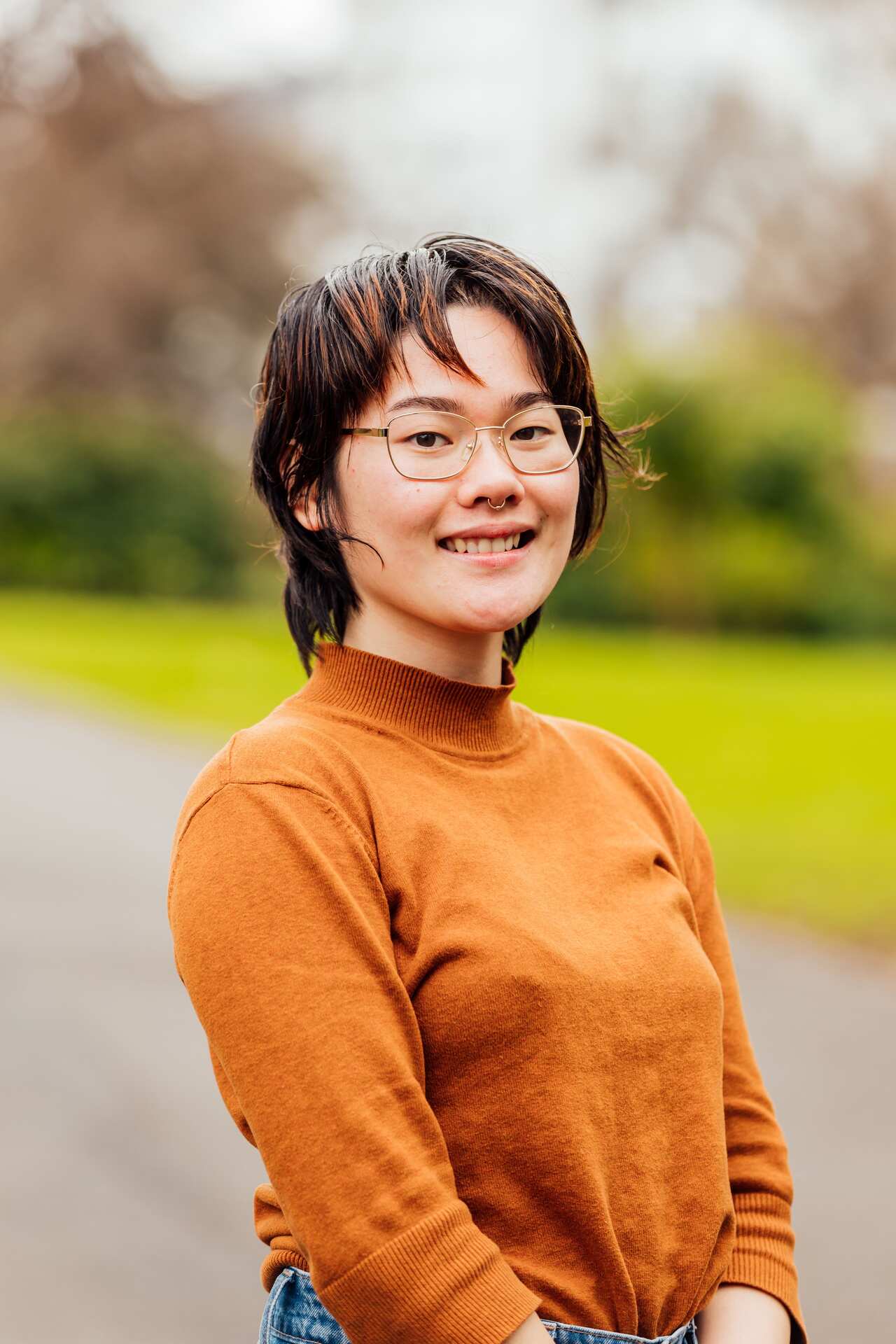 A young person wearing an orange top and glasses smiles at the camera.