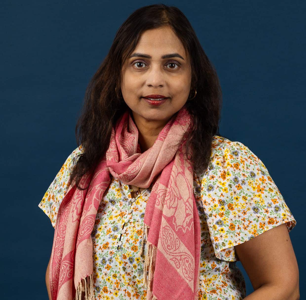 A headshot a woman wearing a floral top and a pink scarf.