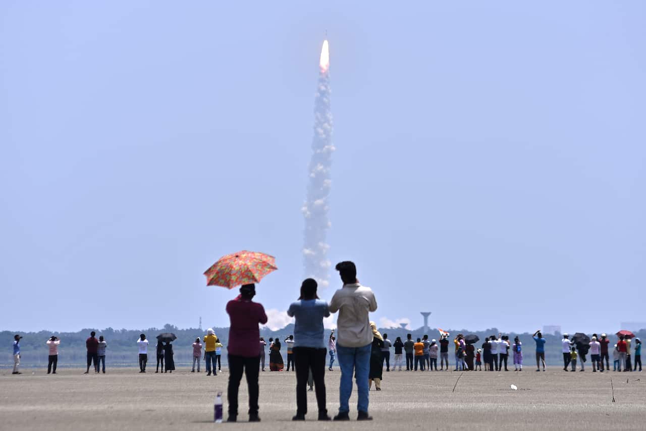 A group of people standing on the ground watch a rocket take off.
