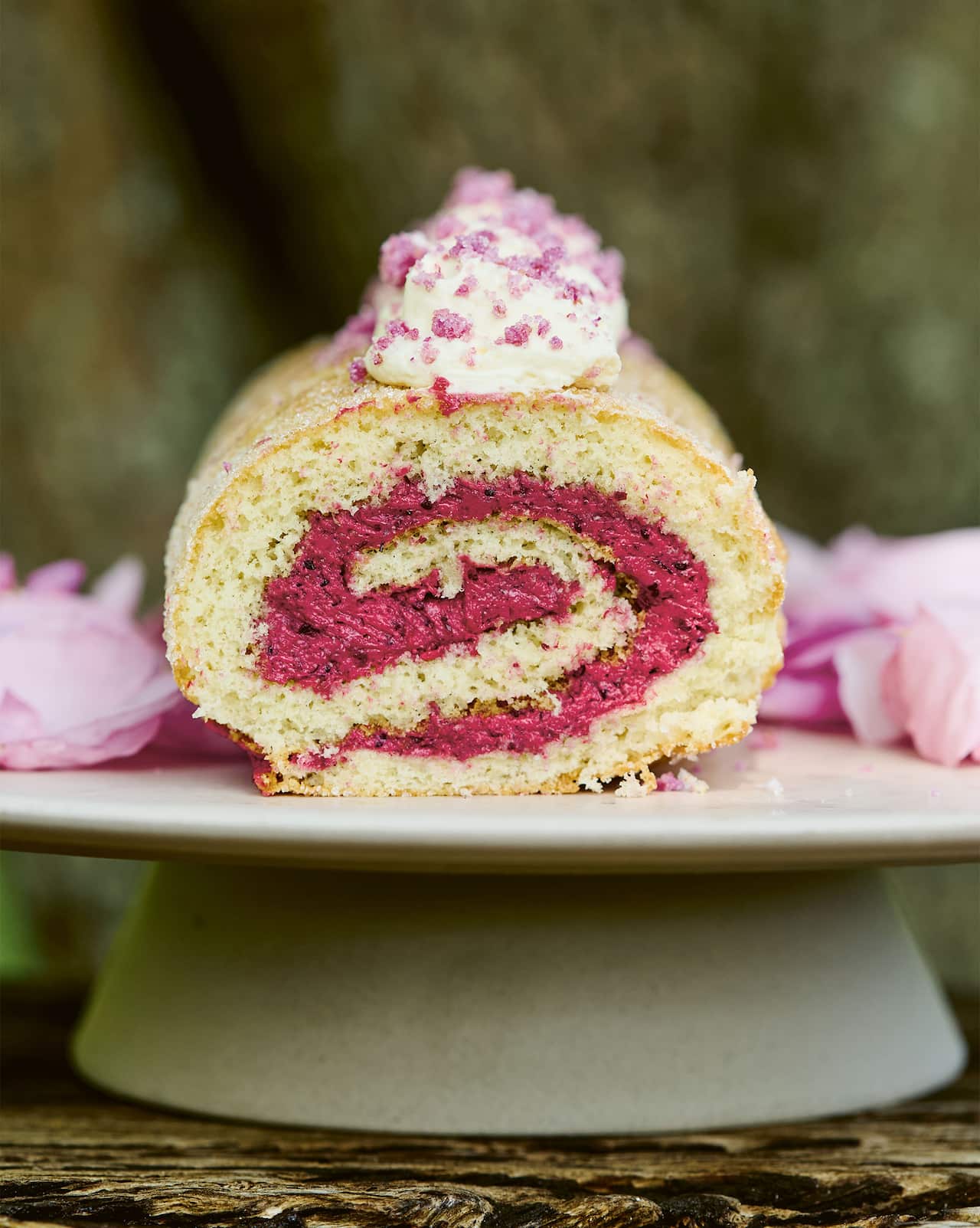 Sponge roulade is filled with a vividly pink blackcurrant jam buttercream, and topped with whipped cream and rose sugar.