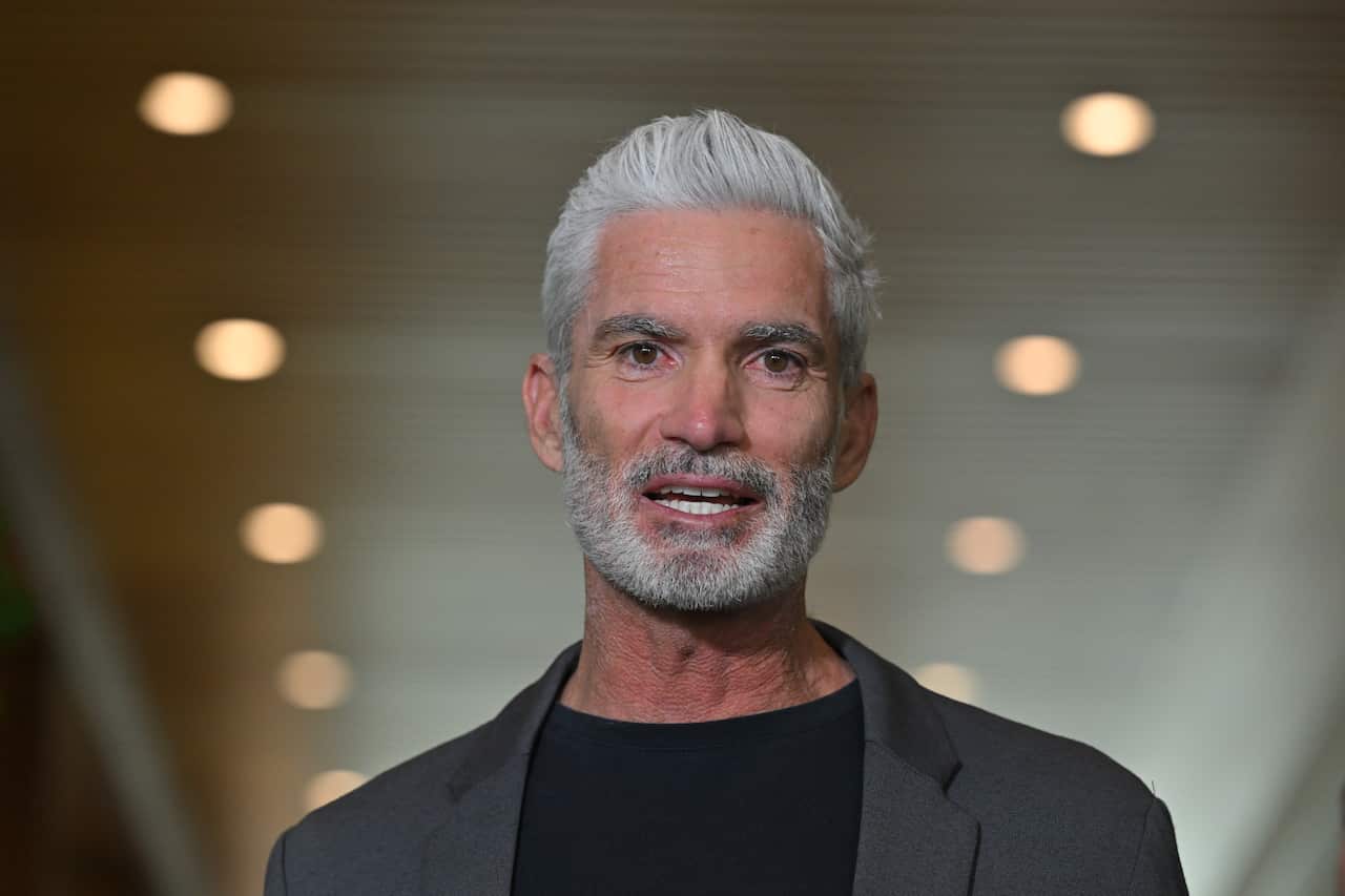 Craig Foster wearing a grey suit with a black shirt underneath.