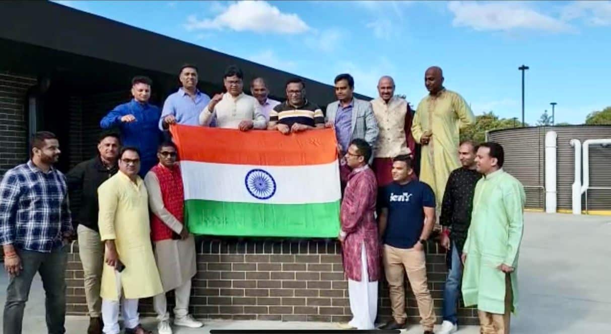 A group of men standing outside. Some of them are holding an Indian flag.
