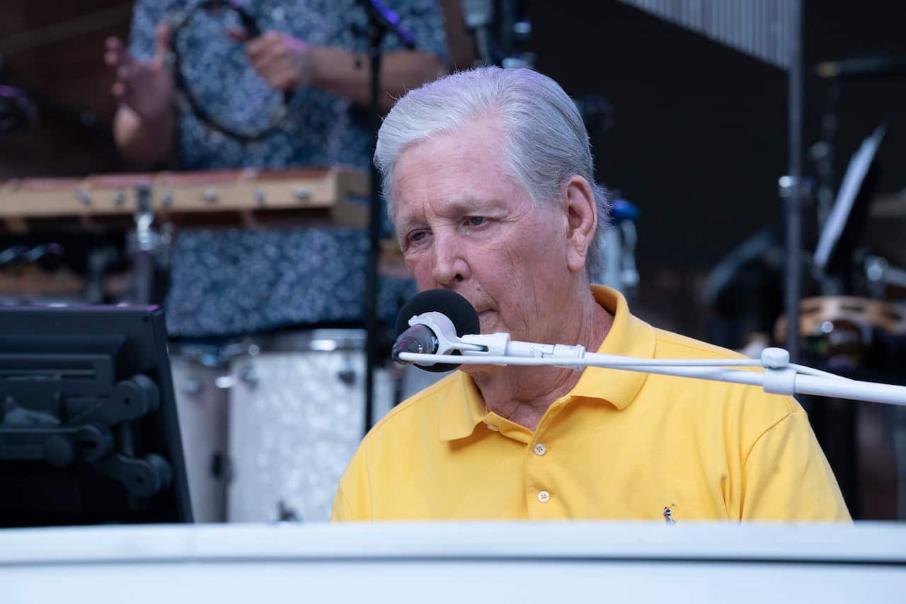 A man wearing a yellow shirt playing piano and singing into a microphone.