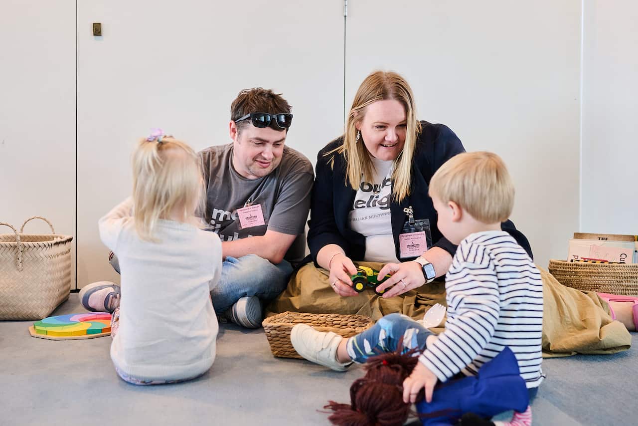 A young family of a woman, a man and two young children play with toys on the floor.
