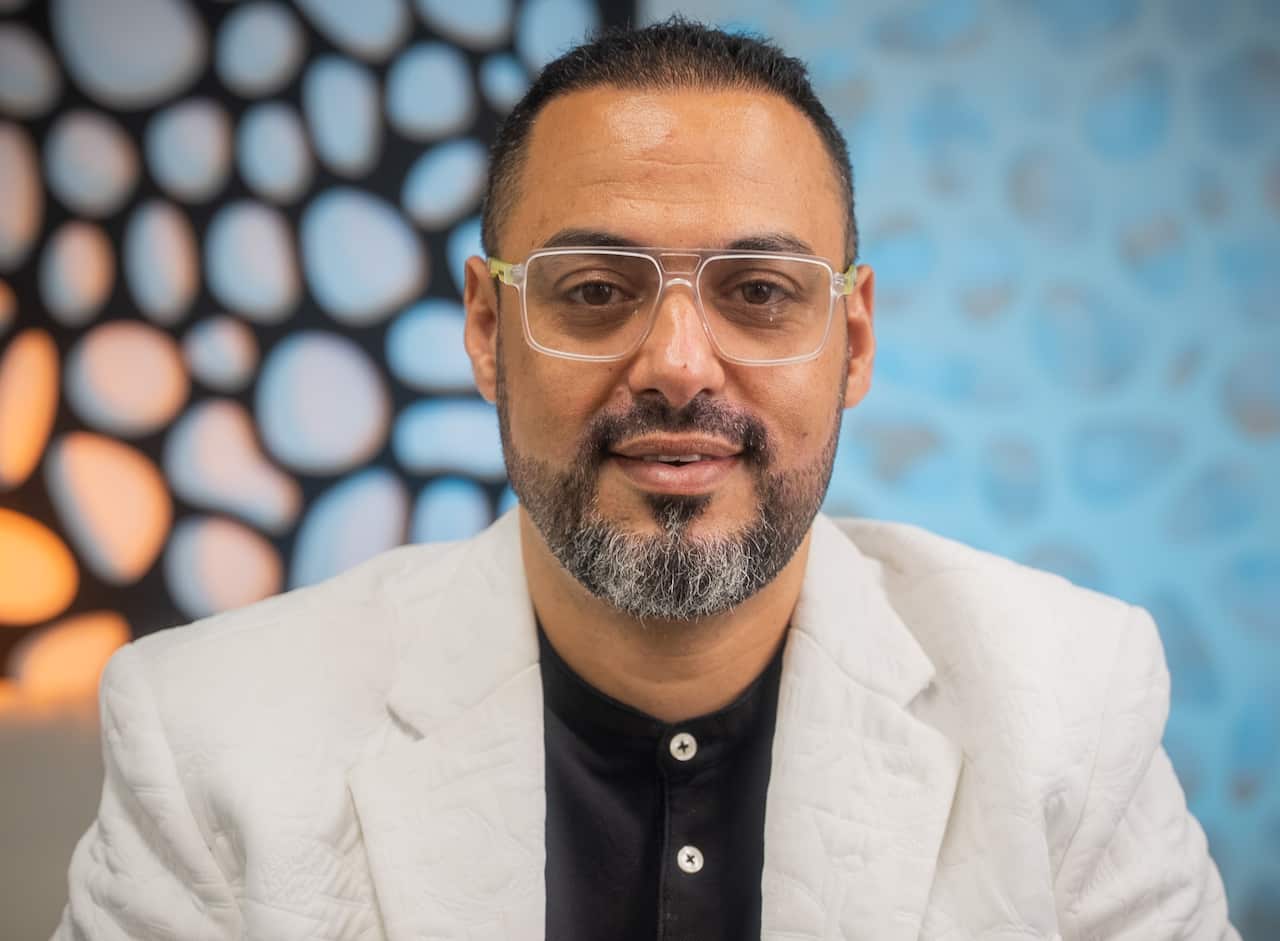 Yasser Zaki in a white jacket and black t-shirt sitting in an office in Sydney. 