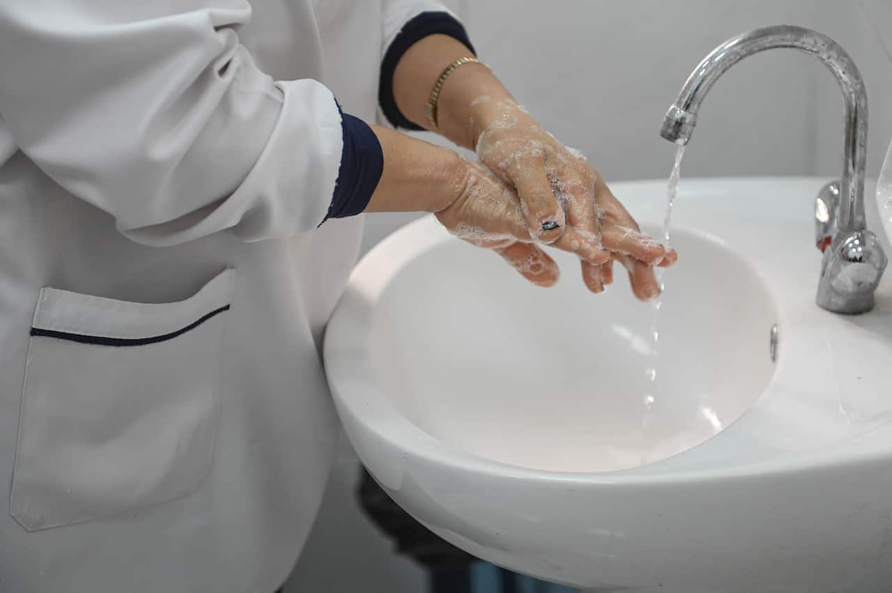 A nurse washes her hands with soap at a wash basin. 
