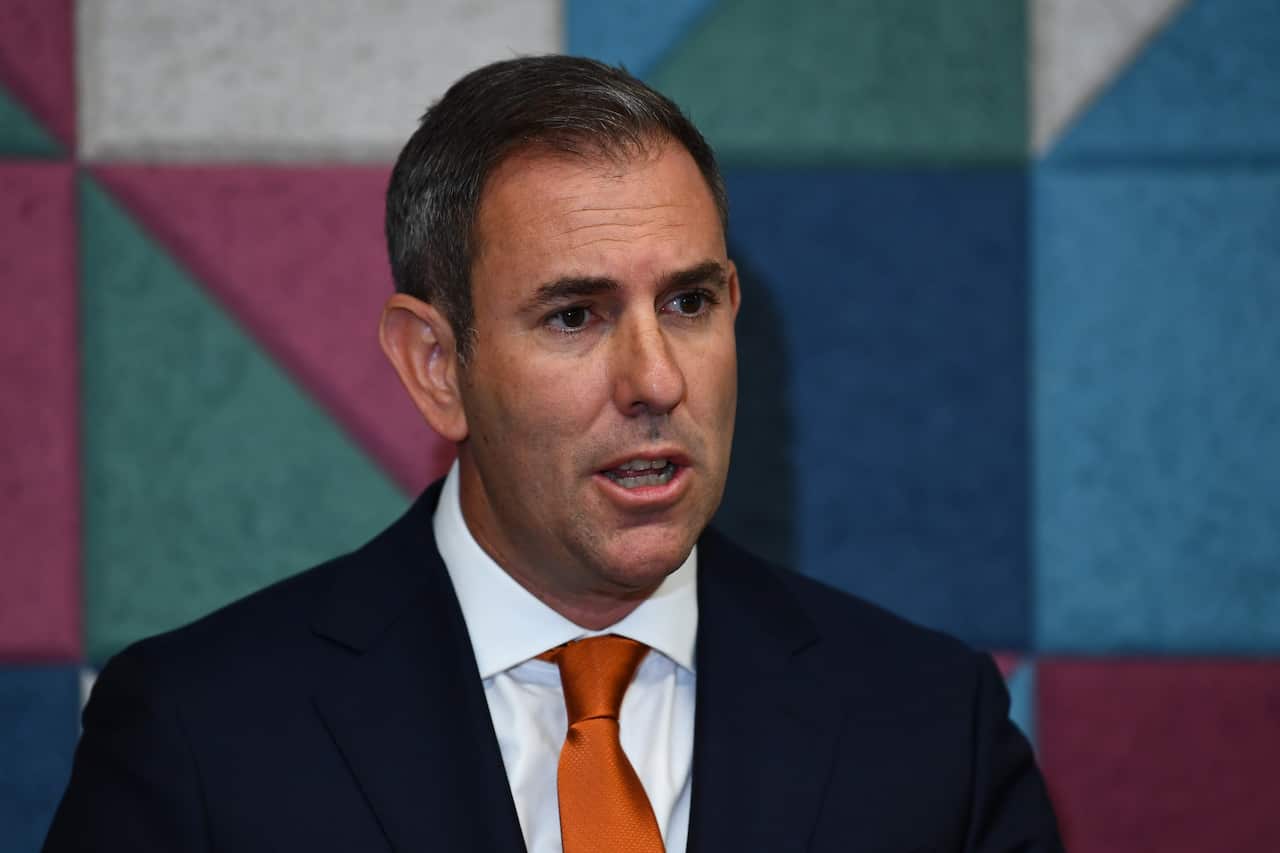 A headshot of the man, Treasurer Jim Chalmers, in an official suit with an orange tie, speaking at a press conference.