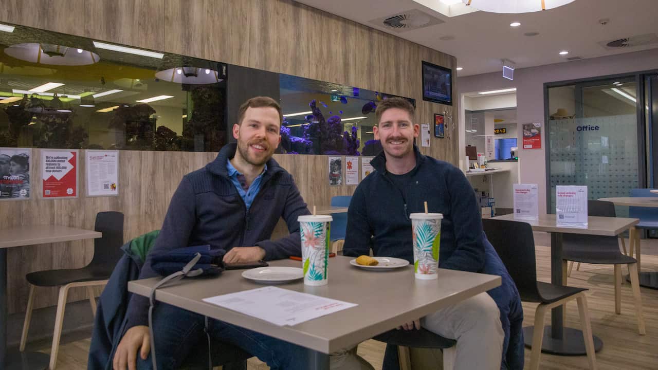 Two men are sitting at a table, with milkshakes and plates in front of them.