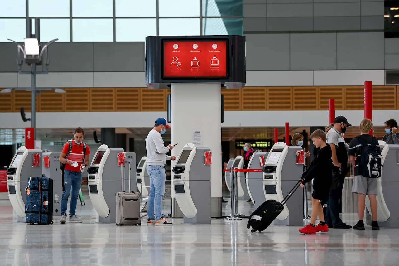 People standing at machines in an airport terminal.