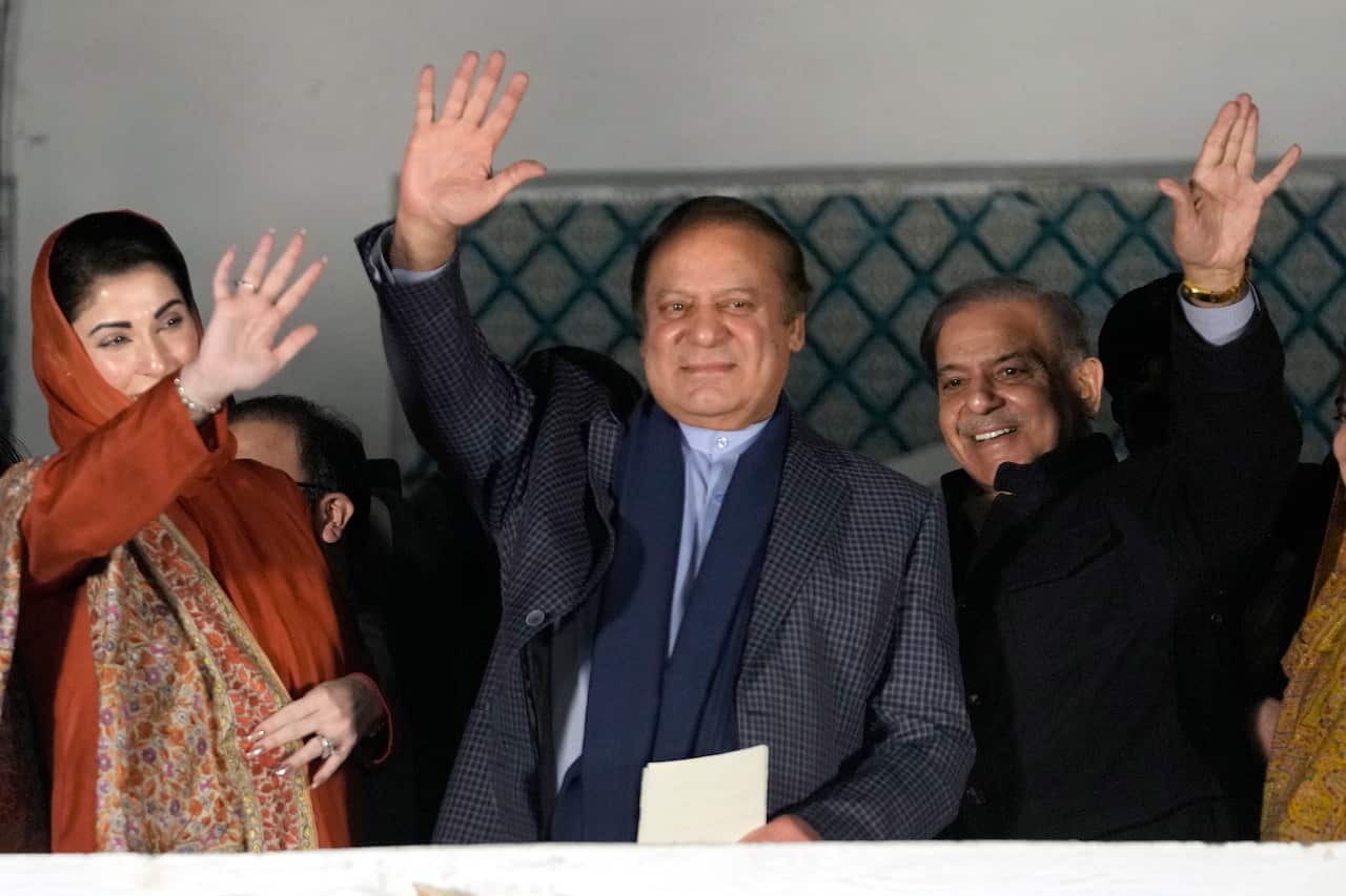 Nawaz Sharif waving and smiling while two supporters next to him wave.
