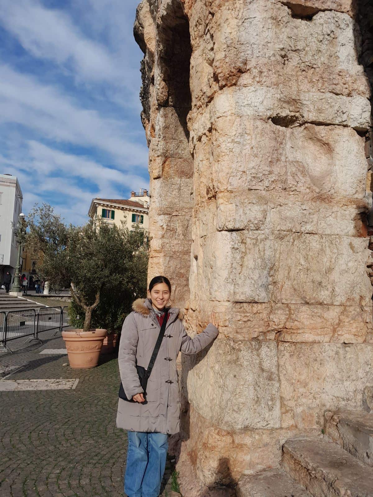 A young woman wearing a winter jacket stands near a rock wall.