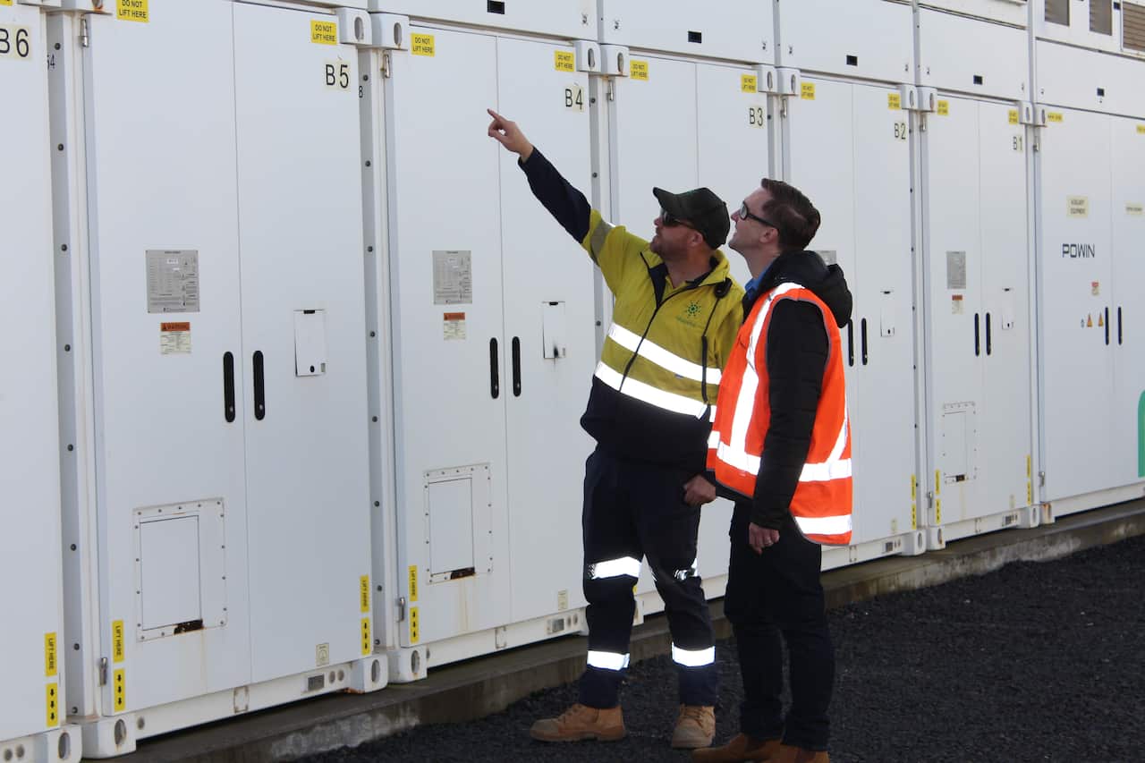 Two men wearing hi-vis vests look at large white cabinets