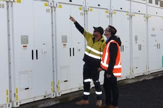 Two men wearing hi-vis vests look at large white cabinets