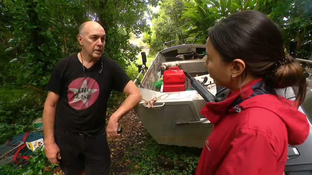 A man leaning against a boat as he speaks to a journalist.