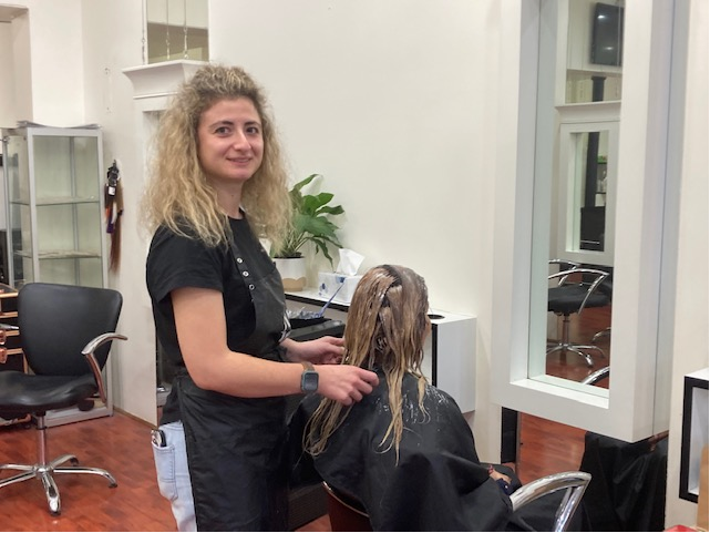 Hairdresser stands while working on a client's hair sitting in a chair. 