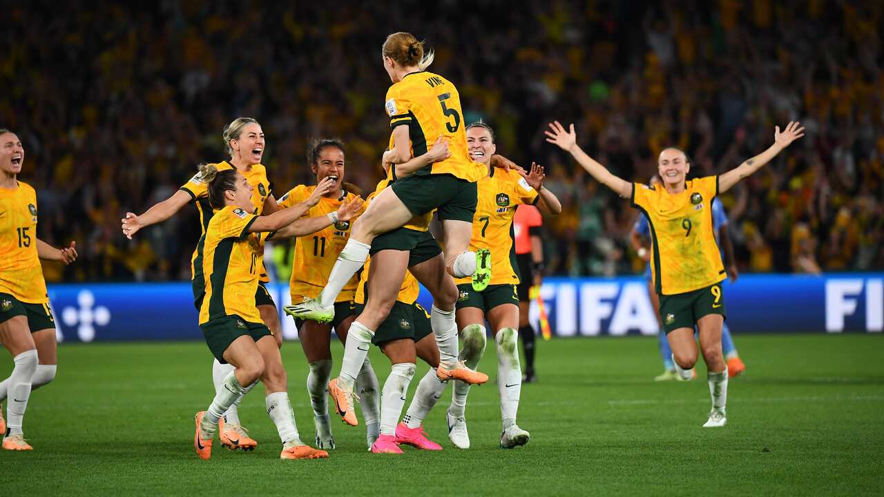 A group of women dressed in football uniforms celebrate on the field. 
