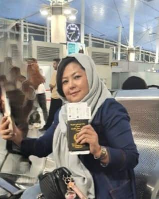 A woman in a navy jacket holds up a passport and tickets while sitting on a boat.
