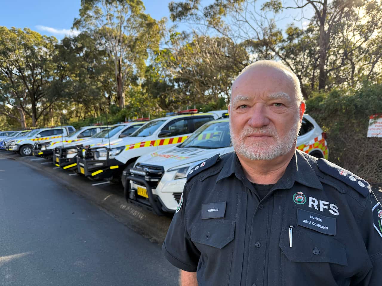 A man wearing an RFS uniform and standing in front of a line of emergency vehicles.