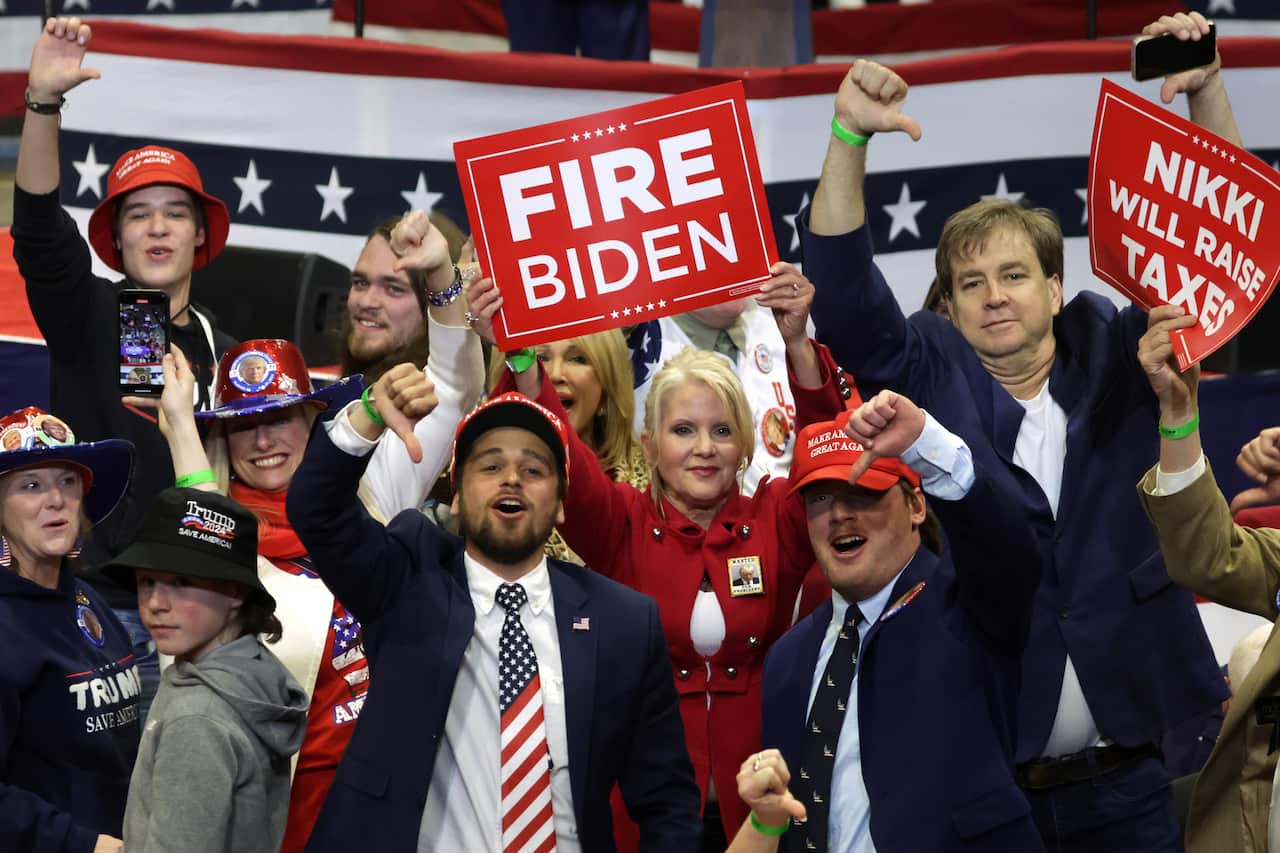 Men and women in a crowd cheering and booing with placards. 