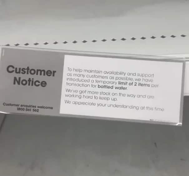 A sign on a shelf at a supermarket notifying customers of restrictions on bottled water sales.