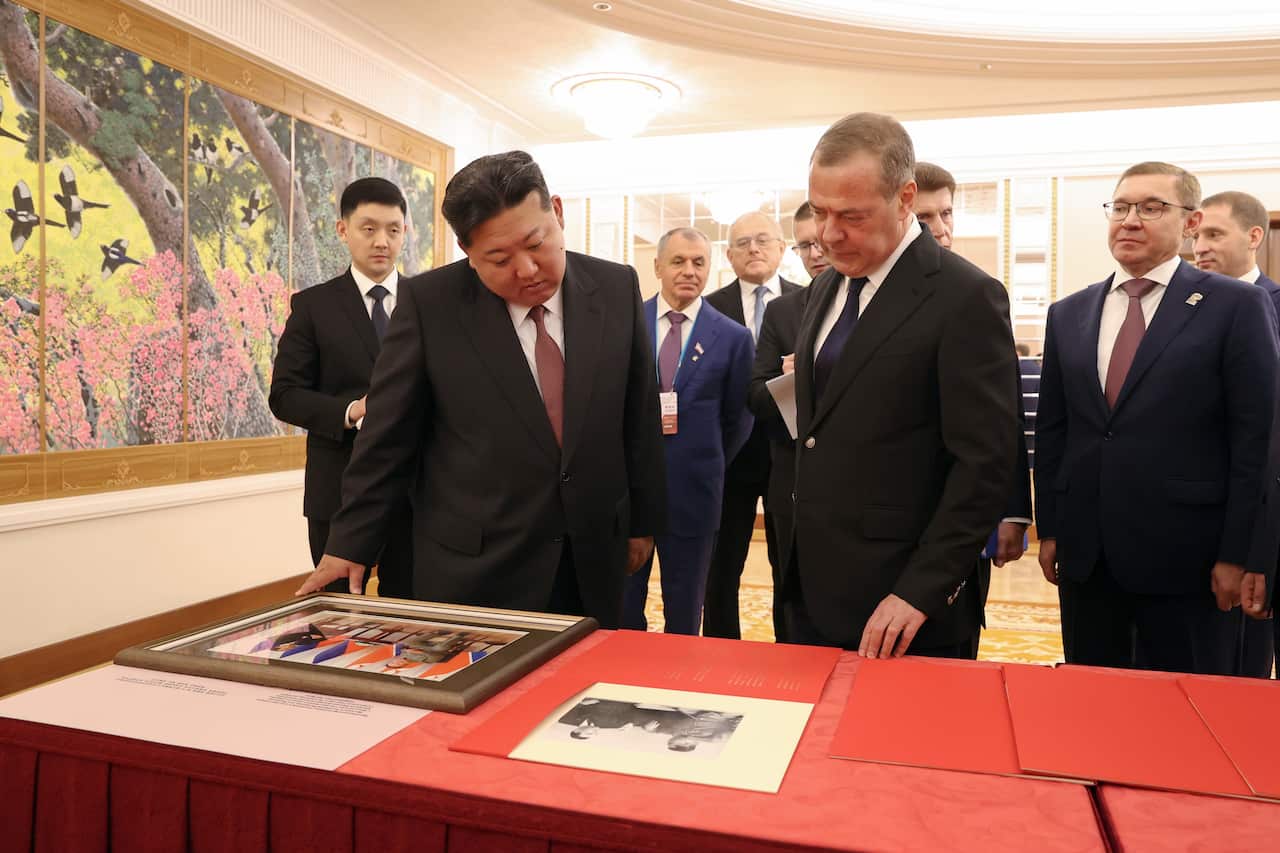 An Asian man and white man wearing suits look over photographs sitting on table 