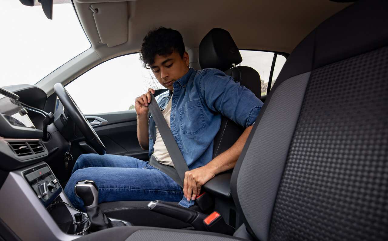 A young man putting on his seatbelt in a right hand side drive car.