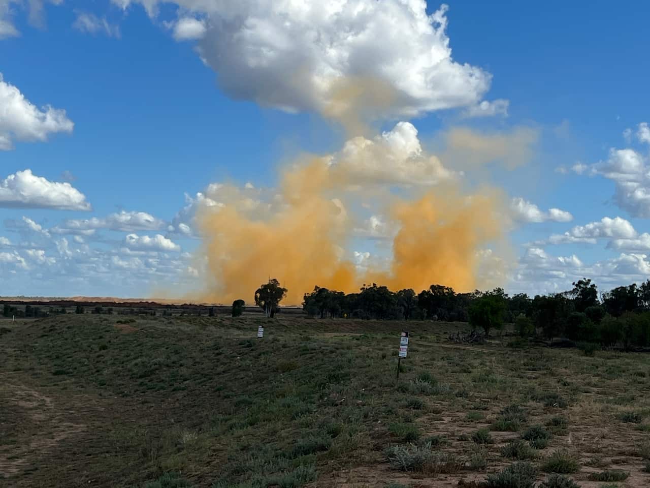 An orange plume of toxic gases rises behind the trees.