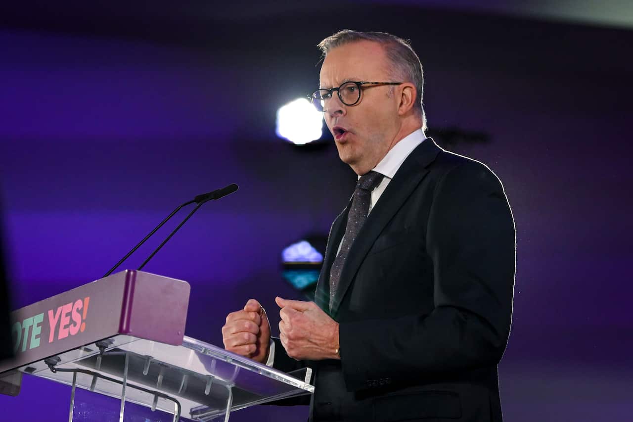 A man in a black suit speaks in front of microphones at a podium.
