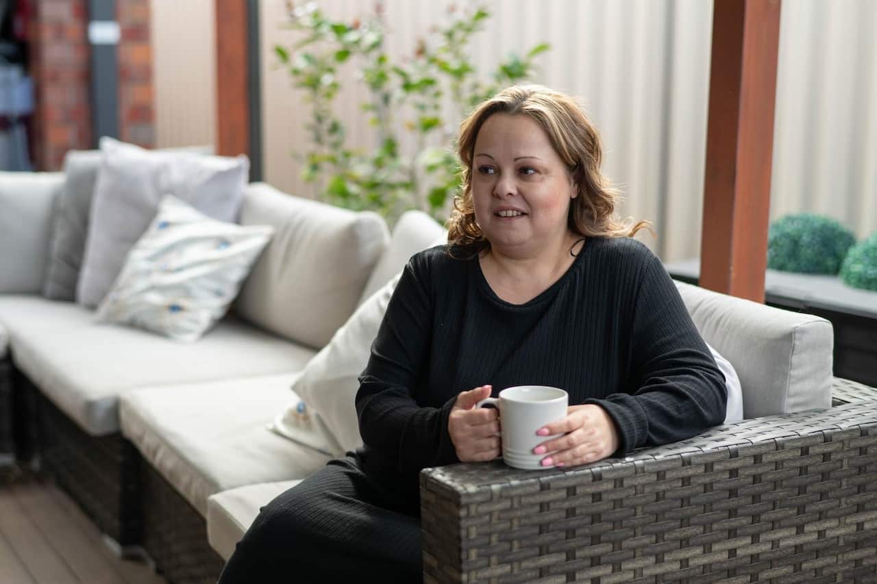 A woman is wearing a black dress and short hair is holding a tea as she poses on an outdoor couch 