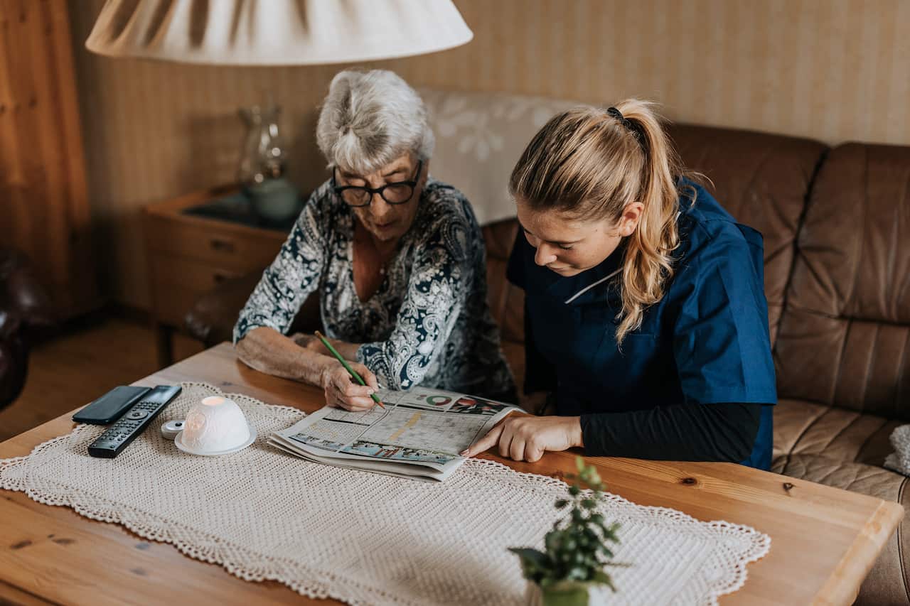 An old woman and a young woman sitting in a living room doing a crossword 