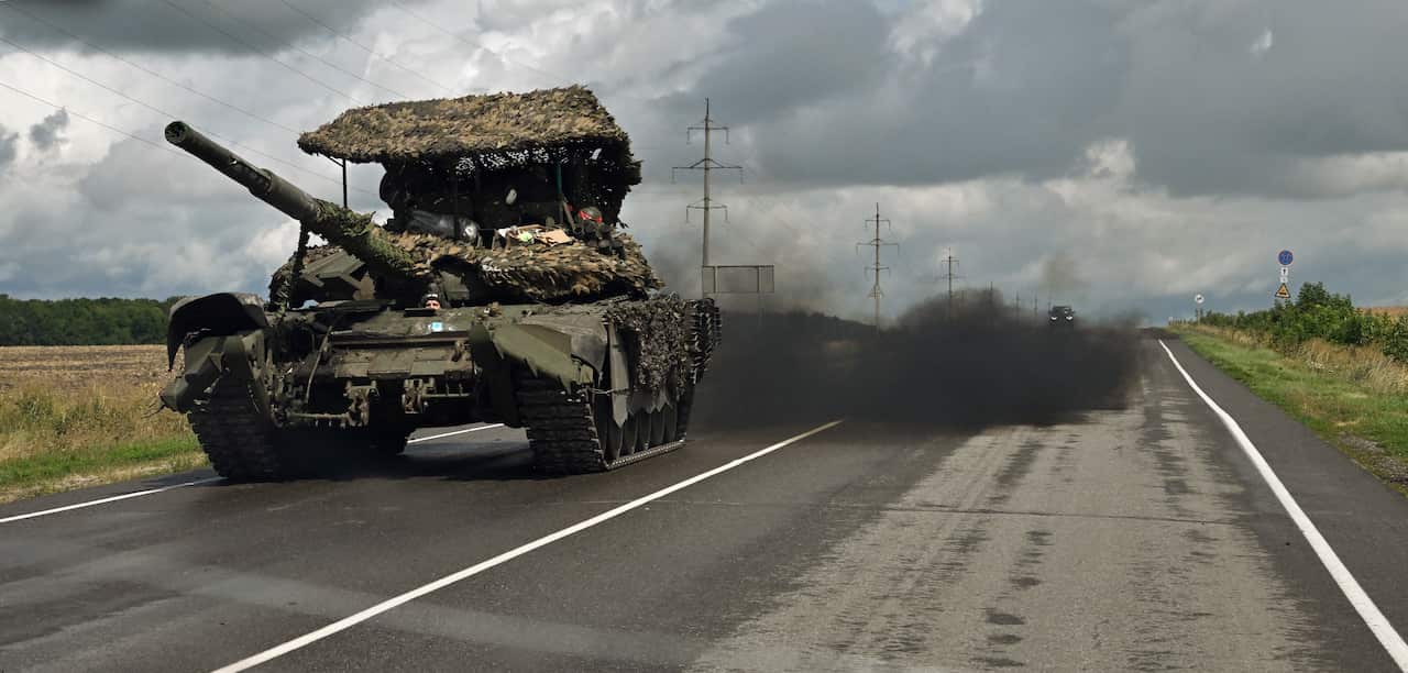 A tank drives down a highway followed by a large plume of black smoke