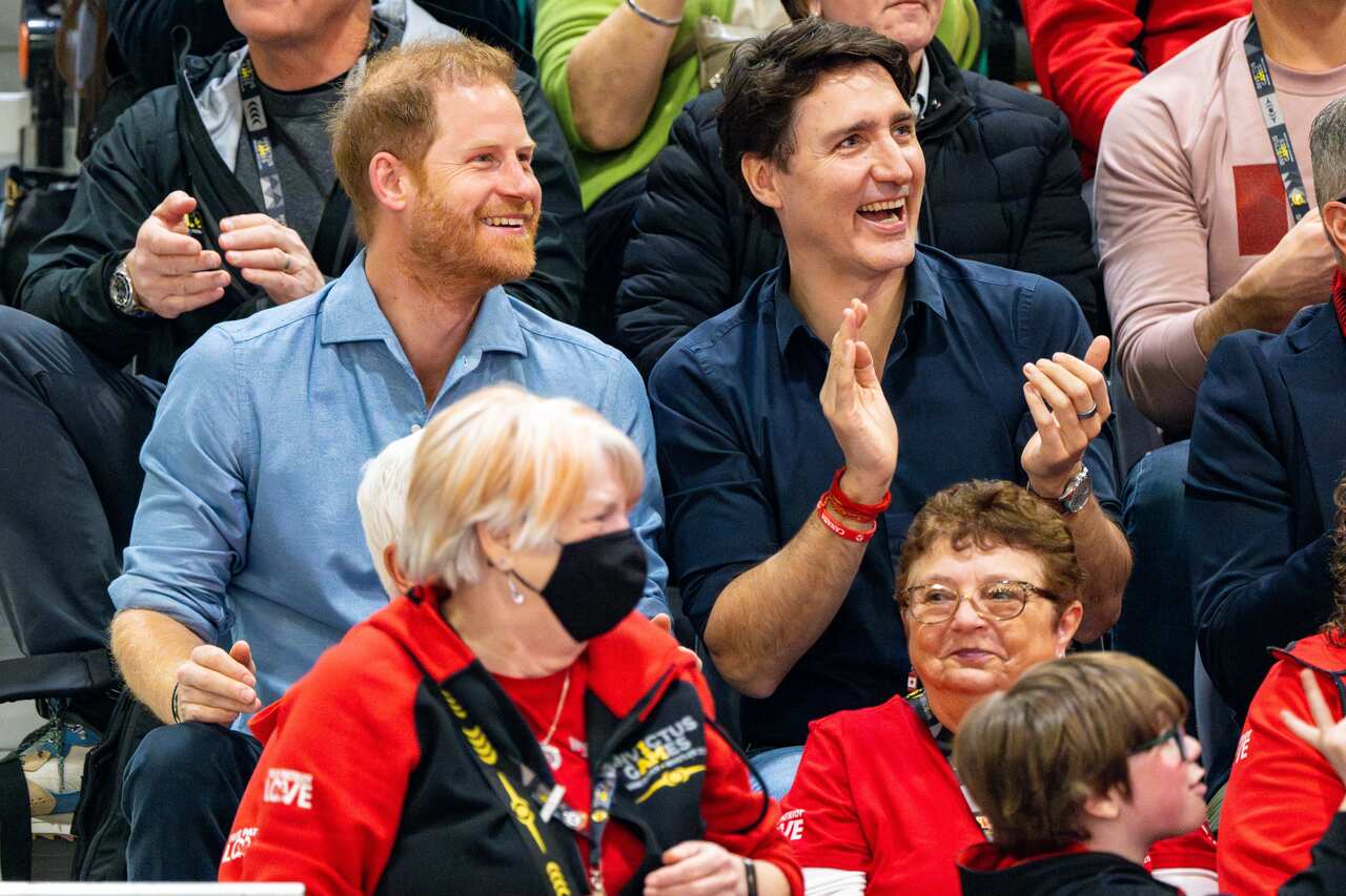Man in a blue shirt smiling next to another man in a dark blue shirt sitting in stadium seats.