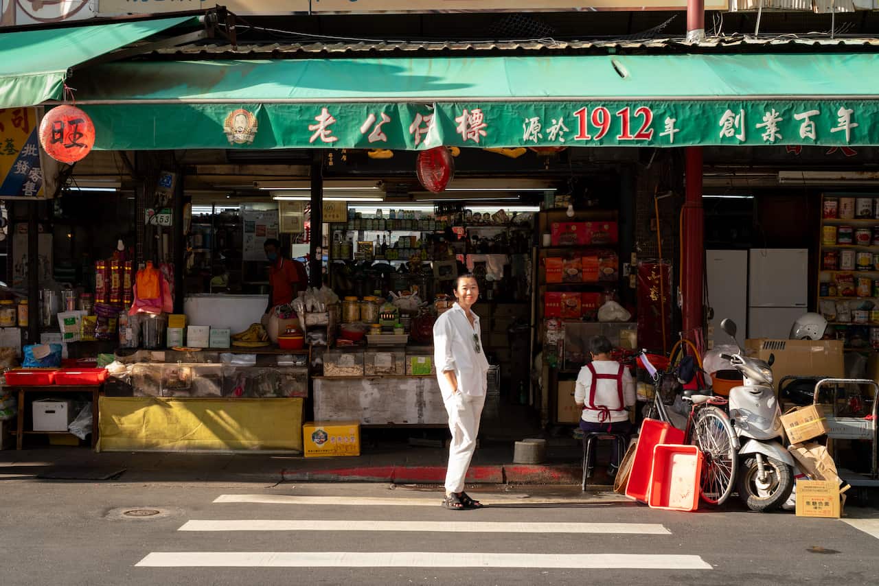 A woman stands at a pedestrian crossing in front of a colourful storefront
