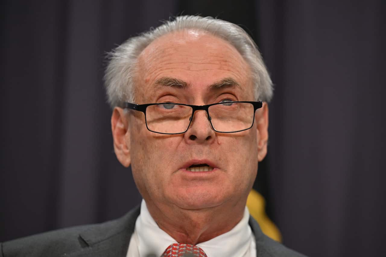 A man in a suit and tie wearing glasses speaks.