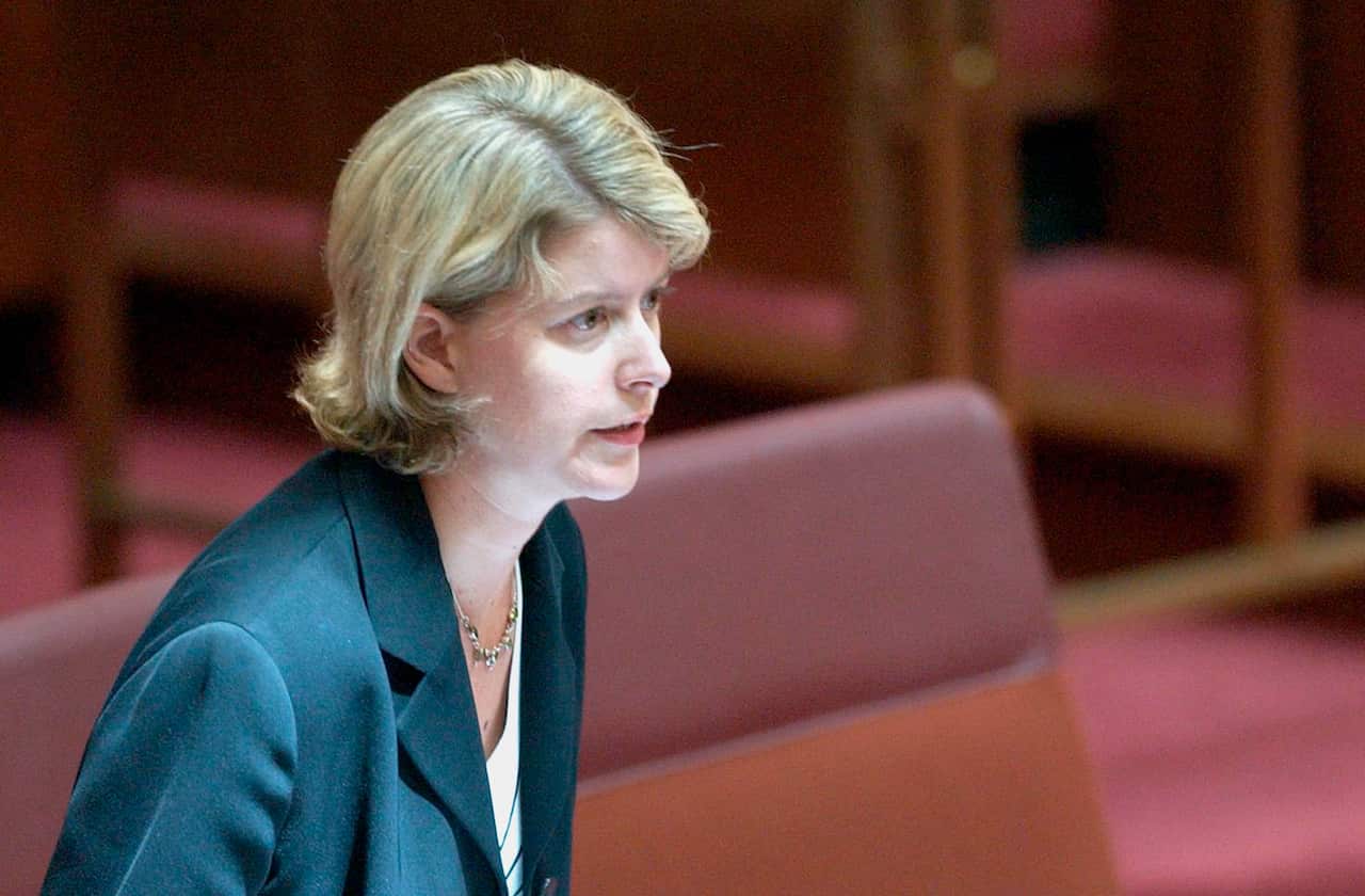 A woman with a blond bob and dark suit stands in the senate chamber