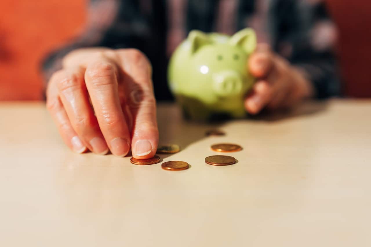 A person holding a piggy bank with one hand and counting some coins with the other.