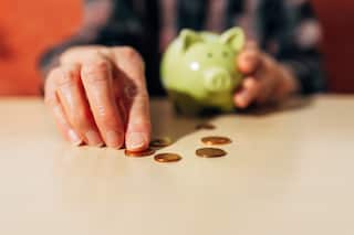 A person holding a piggy bank with one hand and counting some coins with the other.