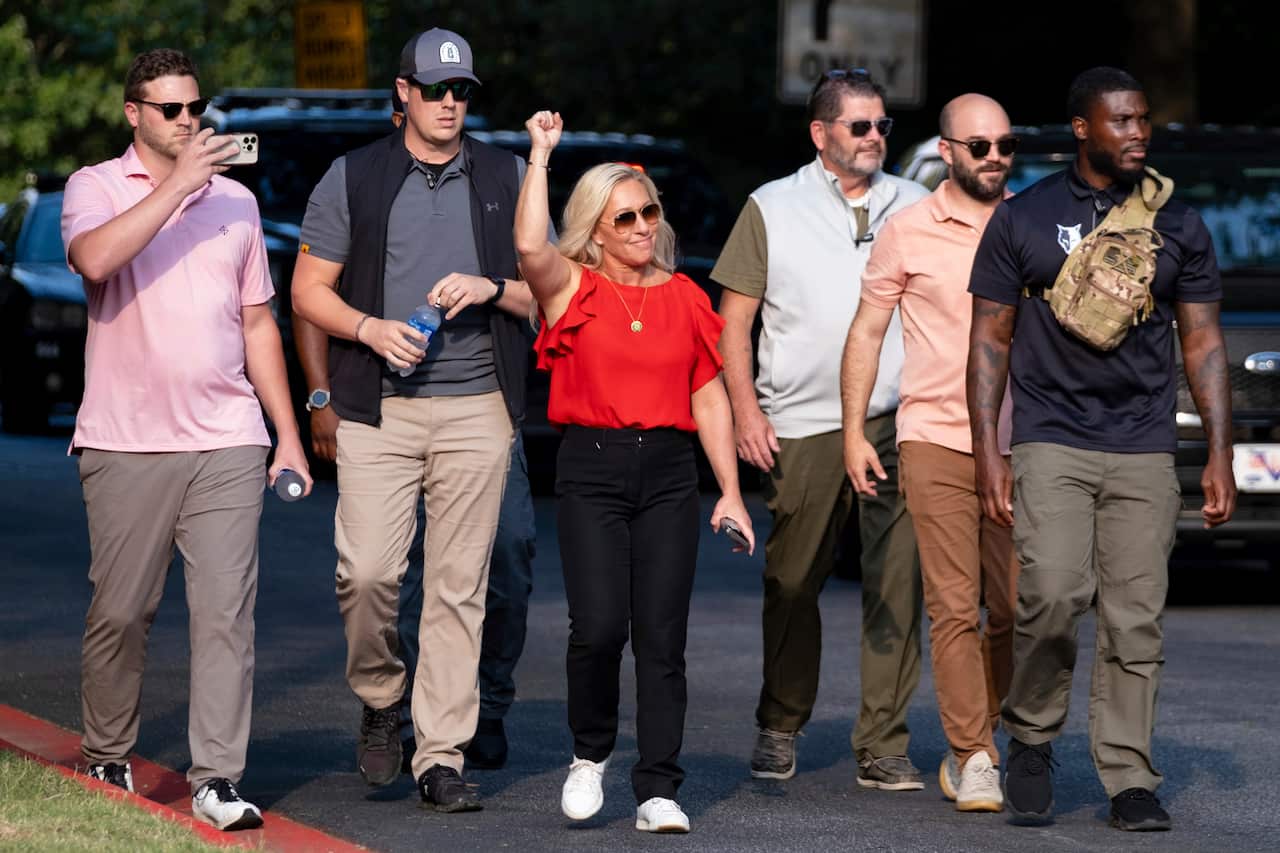 A woman with her hand in the air walking among five other people.