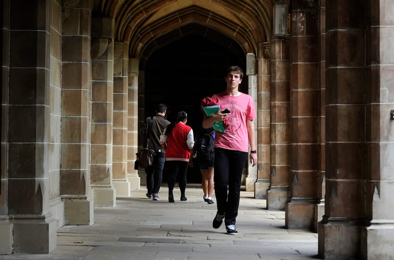 A group of students walking through a stone corridor with high arched ceilings, characteristic of an academic setting.