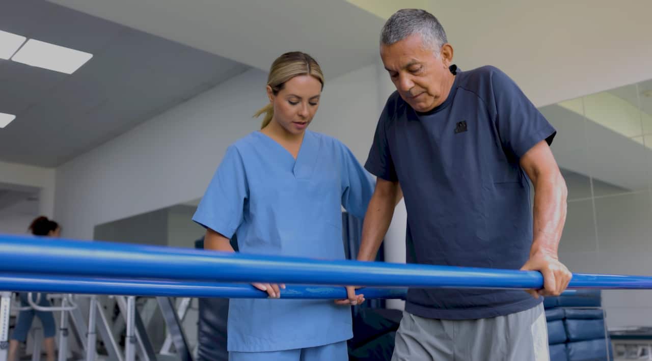 A female therapist standing provides physical rehab to a male patient.