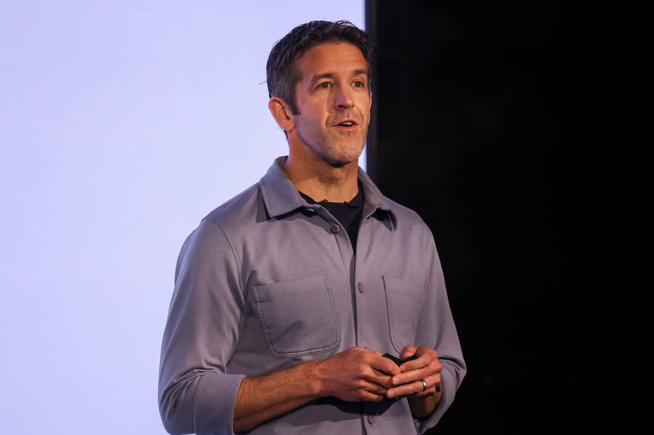 A man wearing a light blue shirt, speaking in front of a purple light.